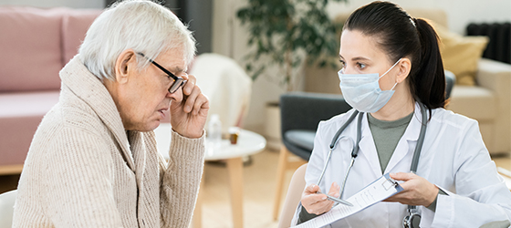 Sick senior man looking through medical document held by young female doctor